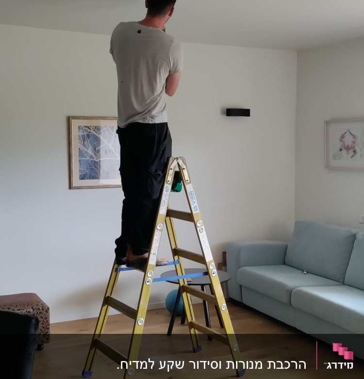 חשמלאי עומד על סולם ומתקין תאורה בתקרה